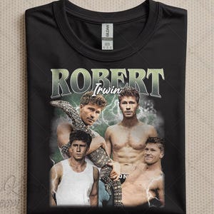 Puede incluir: Camiseta negra con un gráfico de estilo vintage de Robert Irwin. El diseño incluye múltiples imágenes de Irwin, con el nombre "ROBERT Irwin" en una fuente verde desgastada. La camiseta tiene cuello redondo y una etiqueta de la marca "Gildan".