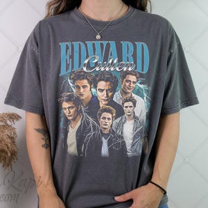 May include: Dark gray t-shirt featuring a collage of images of Edward Cullen from the Twilight saga. The shirt has the text "Edward Cullen" in a blue and silver design, with lightning bolt accents.