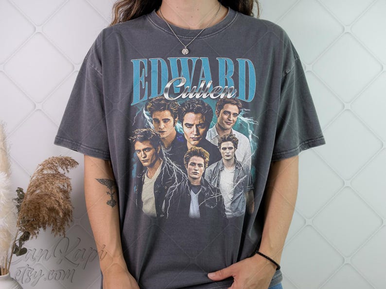 May include: Dark gray t-shirt featuring a collage of images of Edward Cullen from the Twilight saga. The shirt has the text "Edward Cullen" in a blue and silver design, with lightning bolt accents.