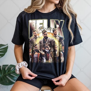 Pode incluir: T-shirt preto com um gráfico de um grupo de homens e o texto "FELIX RICHTER". O design tem uma estética vintage. A camisa está sendo usada. A imagem tem uma aparência desbotada.