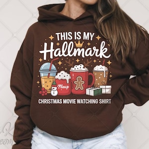 May include: A brown hoodie featuring the text "THIS IS MY Hallmark" and "CHRISTMAS MOVIE WATCHING SHIRT". The design includes festive drink illustrations, a gingerbread man, and a snowman.
