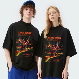 May include: Black t-shirts featuring a Star Wars Episode III graphic with a scene of a lightsaber battle. The text "STAR WARS EPISODE III REVENGE OF THE SITH" is displayed in orange and yellow. The shirts have a mock neck and short sleeves.