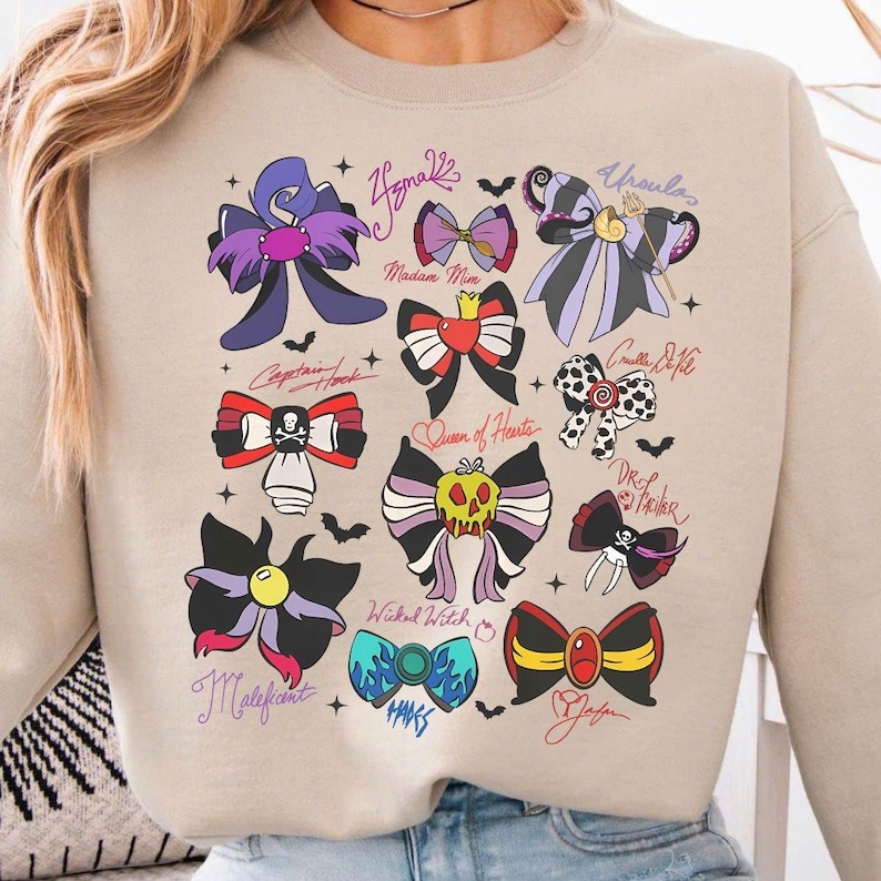 May include: Beige sweatshirt featuring colorful bow designs inspired by Disney villains. Each bow is unique, with names like "Ursula" and "Maleficent" written above them. The bows are in various colors, including purple, red, and black.