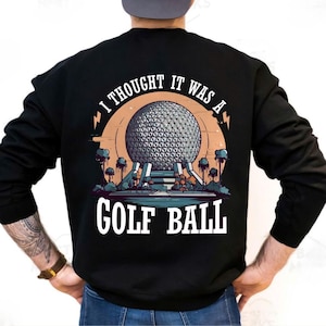 May include: Black sweatshirt with a graphic design featuring a geometric sphere, text that reads "I THOUGHT IT WAS A GOLF BALL", and a landscape scene. The design is in shades of gray, orange, and blue.