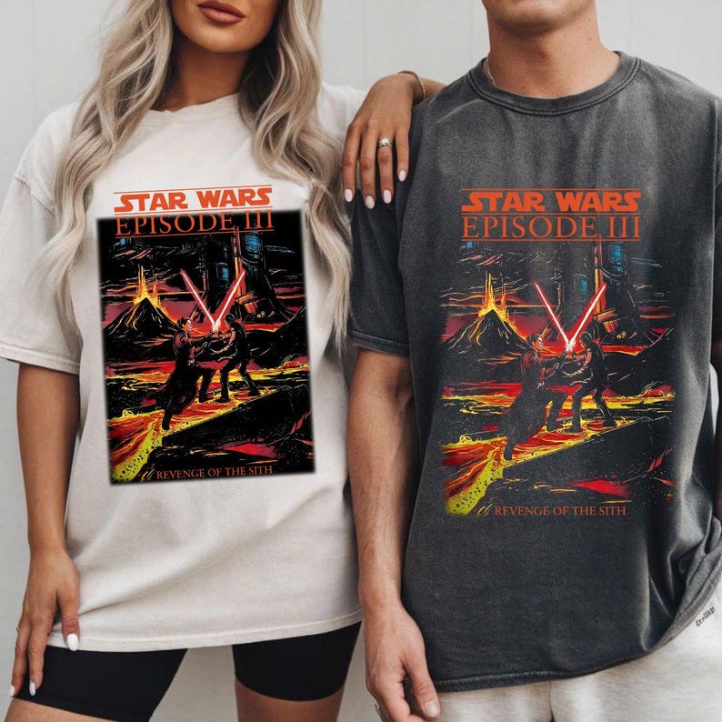 May include: Two t-shirts featuring the Star Wars Episode III: Revenge of the Sith movie poster. The design includes a red and orange color scheme with two figures wielding red lightsabers. One shirt is off-white, the other is dark gray.