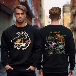 Peut inclure: Sweat-shirt noir avec un motif de "Le Roi Lion". L'avant présente une tête de lion stylisée avec des personnages et des motifs. Le dos montre une illustration en forme de carte avec du texte et des images du film.