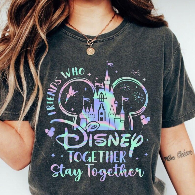 May include: Dark gray t-shirt featuring a holographic Disney castle design with the text "Friends Who Disney Together Stay Together." The design includes fireworks, balloons, and a fairy. The shirt is a comfortable, casual wear item.
