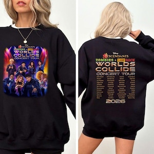 May include: A black long-sleeve sweatshirt featuring a graphic print of the Disney Descendants Zombies + Camp Rock Worlds Collide Concert Tour. The front displays a cast photo under stage lights, while the back lists tour cities and the year 2026.