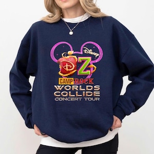 Może przedstawiać: Granatowa bluza z nadrukiem graficznym. Projekt zawiera napis "Camp Rock Worlds Collide Concert Tour", stylizowane jabłko, logo Disneya i literę "Z" w kolorze zielonym. Bluza ma okrągły dekolt.