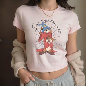 May include: A light pink t-shirt featuring a cartoon illustration of two chipmunks dressed as wizards. The top chipmunk wears a blue wizard hat and holds a wand. The text "Some imagination huh?" is above the chipmunks.