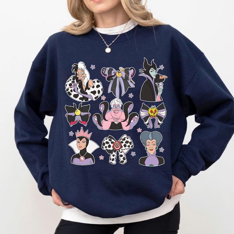 Op de afbeelding: Marineblauw sweatshirt met kleurrijke cartoon illustraties van verschillende schurken. De afbeeldingen bevatten Cruella de Vil, Ursula en de boze koningin, en meer. Het ontwerp is tegen een donkerblauwe achtergrond.