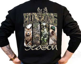 May include: Black long-sleeve sweatshirt with a hunting theme. The back features the words "HUNTING SEASON" in camouflage lettering, with images of a deer, binoculars, and a duck.