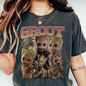 May include: Dark gray t-shirt featuring the word "GROOT" in a gradient orange and brown font. The shirt displays a graphic of several Groot characters from the Guardians of the Galaxy movies. The characters are in various poses and sizes.