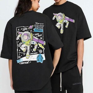 May include: Black t-shirts featuring a Buzz Lightyear graphic from Disney Pixar's Toy Story. The design includes the text "Toy Story", "Galactic Hero!", "Buzz Lightyear", and "Space Ranger". The graphic is in shades of green, purple, white, and blue.