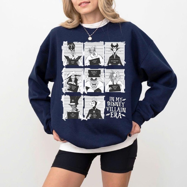 May include: Navy blue sweatshirt featuring a graphic of Disney villains in mugshot-style frames. The text "IN MY DISNEY VILLAIN ERA" is printed in white. The sweatshirt is a crew neck style.