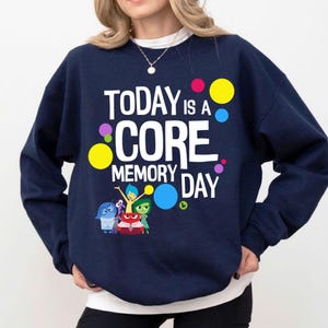 May include: A navy blue sweatshirt with the white text "TODAY IS A CORE MEMORY DAY". The design includes colourful circles and cartoon characters from the film "Inside Out".
