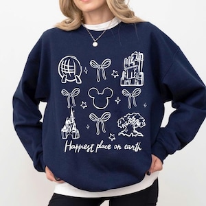 Könnte beinhalten: Marineblaues Sweatshirt mit weißen grafischen Symbolen von Globus, Schleifen, Mickey Mouse, einem Schloss und einem Baum. Der Text "Happiest place on earth" ist in weißer Schrift darunter gedruckt.