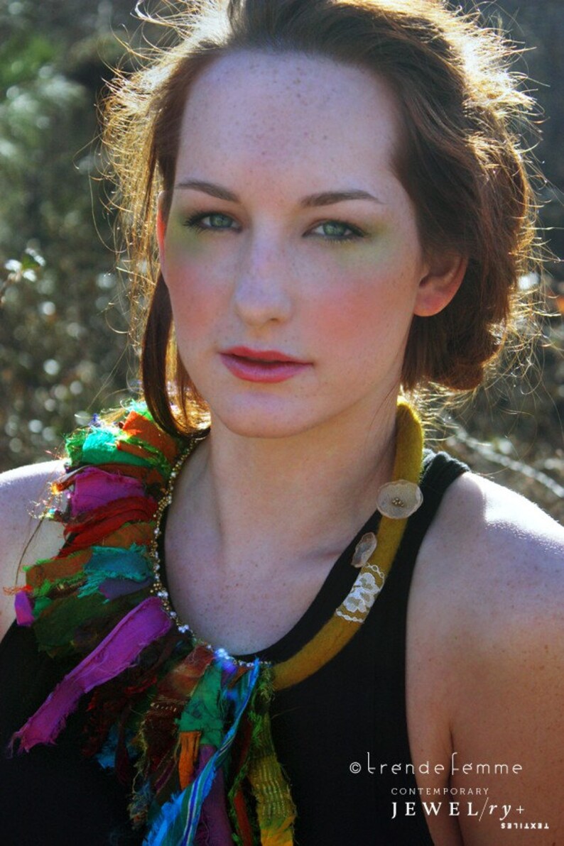Puede incluir: Una mujer con el pelo largo y casta&ntilde;o lleva un top negro de tirantes y un collar de tela colorido y de capas. El collar est&aacute; hecho de tiras de tela en varios tonos de verde, azul, morado y rojo. El collar est&aacute; atado con un cord&oacute;n marr&oacute;n y tiene un ribete de encaje blanco.
