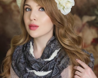 Puede incluir: Una mujer con una corona de flores de rosas blancas y una bufanda estampada con detalles blancos. La bufanda está drapeada alrededor del cuello y los hombros. La mujer lleva un top de encaje rosa claro.