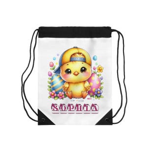 Puede incluir: Bolsa con cordón blanca con un pollito de dibujos animados con una gorra de béisbol amarilla y azul. El pollito está rodeado de huevos de Pascua y flores. El nombre "SOPHIA" está impreso en rosa en la parte inferior.