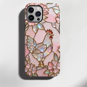 May include: A phone case featuring a stained-glass design with a rooster and floral elements. The case has a pink background with gold-colored outlines and iridescent accents. The rooster has a red comb and wattle.