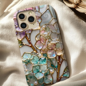 May include: A decorative phone case featuring a floral design with pastel colors. The case has a white background with gold-colored outlines and iridescent accents. The design includes purple, pink, and teal flowers with pearl-like embellishments.