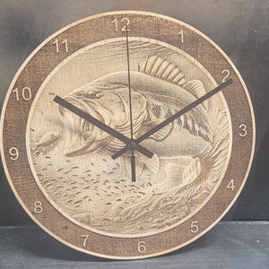 May include: A wooden clock with a brown background and black hands. The clock face features a detailed carving of a largemouth bass with smaller fish surrounding it. The numbers 1 through 12 are displayed around the edge of the clock face.