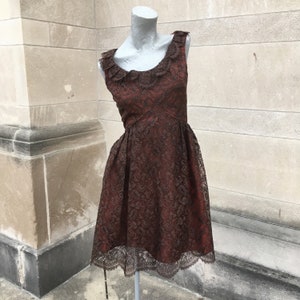 Puede incluir: Un vestido de encaje marrón con un escote festoneado y un corpiño ajustado. El vestido tiene una falda completa y es sin mangas.