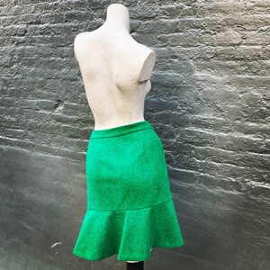 Pu&ograve; includere: Una gonna verde con orlo svasato. La gonna &egrave; realizzata in tessuto strutturato e ha un design semplice.