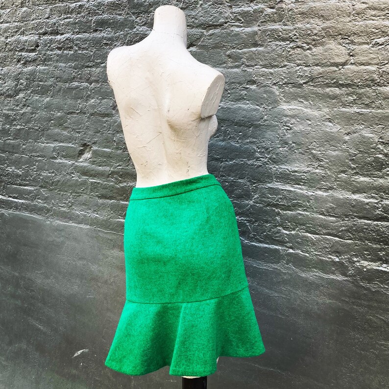 Pu&ograve; includere: Una gonna verde con orlo svasato. La gonna &egrave; realizzata in tessuto strutturato e ha un design semplice.