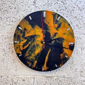 Puede incluir: Reloj de pared redondo con un diseño abstracto en negro y naranja. La esfera del reloj tiene manecillas negras, un segundero rojo y marcadores de hora plateados. Montado en una pared blanca texturizada.