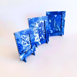 Puede incluir: Tres marcos de fotos de mármol azul y blanco, cada uno con un soporte. Los marcos son rectangulares con una abertura rectangular más pequeña. Los marcos están hechos de un material con un patrón arremolinado de azul y blanco.