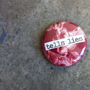 May include: A red button with a white label that says "tells lies" on it. The button has a floral pattern.