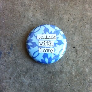 May include: A blue and white button with the text "think with love" printed on it.