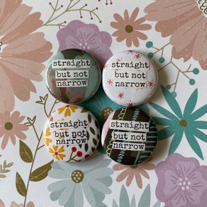 May include: Four round buttons with the text "straight but not narrow" in white. The buttons have different patterned backgrounds, including floral and abstract designs. The buttons are arranged on a floral patterned background.