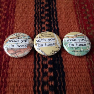 Puede incluir: Tres botones redondos con un diseño de mapa y el texto "with you I'm home" en cada botón.