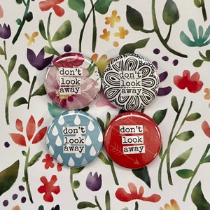 May include: Four 1.25 inch button pins with a white background and black text that reads "don't look away". Each pin has a different design: floral, doodle, raindrops, and arrows.