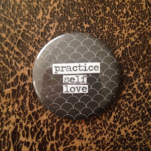 May include: Black and white button with a pattern of overlapping circles. The button has the text "practice self love" printed on it.