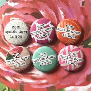 Puede incluir: Seis botones redondos con fondo blanco y texto negro que dice "MOM upside down is WOW". Cada botón tiene un patrón colorido diferente en el fondo.