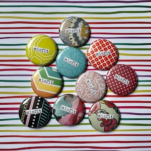 Peut inclure: Neuf boutons ronds avec une variété de motifs colorés et le mot "misfit" imprimé en noir sur chaque bouton.
