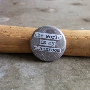 May include: A gray button with white polka dots and the text "the world is my classroom" printed in black.