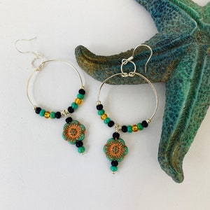 May include: A pair of silver hoop earrings with turquoise and gold beads. Each earring has a turquoise flower charm dangling from it.