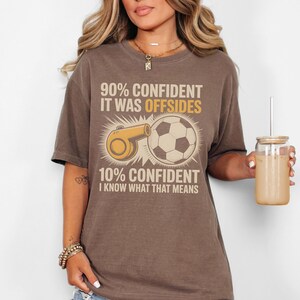 May include: Brown t-shirt with the text "90% CONFIDENT IT WAS OFFSIDES 10% CONFIDENT I KNOW WHAT THAT MEANS." The graphic includes a soccer ball and a referee whistle.
