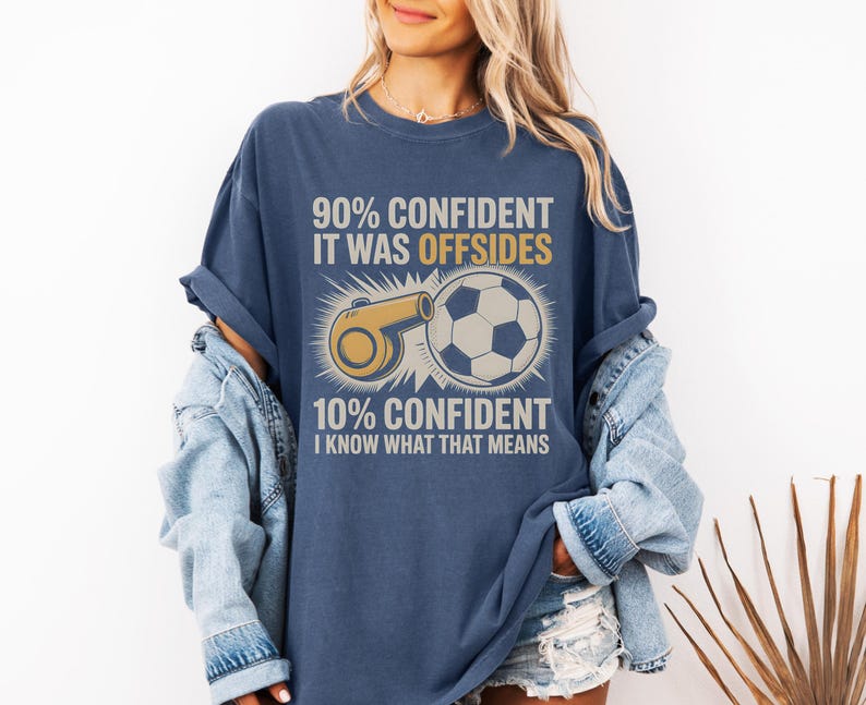 May include: Navy blue t-shirt with a soccer theme. The shirt features a graphic of a soccer ball and a whistle, along with the text "90% CONFIDENT IT WAS OFFSIDES" and "10% CONFIDENT I KNOW WHAT THAT MEANS."