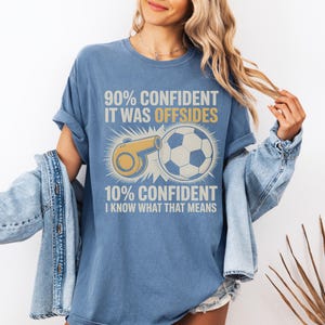 May include: Blue t-shirt with the text "90% CONFIDENT IT WAS OFFSIDES" and "10% CONFIDENT I KNOW WHAT THAT MEANS". The shirt features a soccer ball and a whistle graphic in yellow and white.