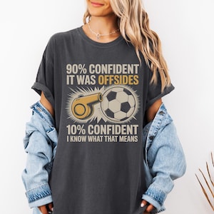 May include: Dark gray t-shirt with a soccer theme. The shirt features a graphic of a soccer ball and a whistle, along with the text "90% CONFIDENT IT WAS OFFSIDES" and "10% CONFIDENT I KNOW WHAT THAT MEANS."
