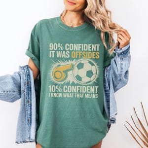 May include: Green t-shirt with a soccer theme. The shirt features a soccer ball and a referee whistle graphic, along with the text "90% Confident It Was Offsides" and "10% Confident I Know What That Means."