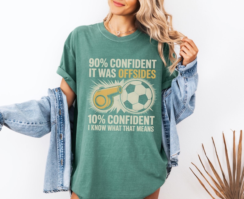 May include: Green t-shirt with a soccer theme. The shirt features a soccer ball and a referee whistle graphic, along with the text "90% Confident It Was Offsides" and "10% Confident I Know What That Means."