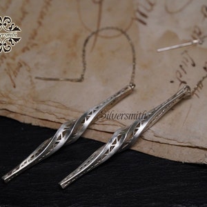 Puede incluir: Un par de pendientes de plata con un diseño retorcido y calado. Los pendientes están suspendidos de una cadena delicada.