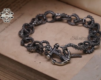 May include: A silver bracelet with an anchor clasp and an octopus tentacle design. The bracelet is made of metal and has a dark, oxidized finish.